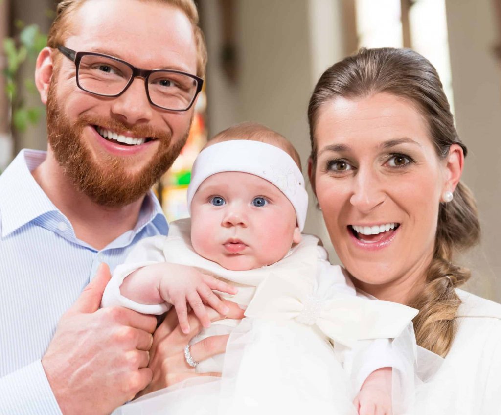 Young parents kiss their baby at the same time after the christening ceremony